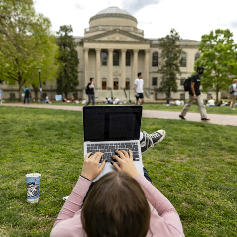 Student using their computer on the quad facing Wilson Library.